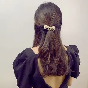 Detail view of a pearl bow hair clip elegantly styled on a model's half-up dark brown hair