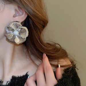 Close-up of a large silver metallic flower earring with a pearl center on a female model