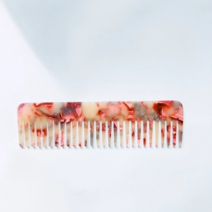 Detailed view of wide-tooth acetate hair comb with pink and beige terrazzo patterns
