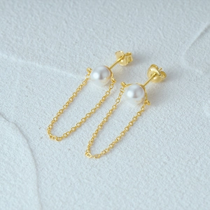 Close-up of elegant gold plated silver earrings with round pearls and delicate chain fringe