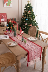 Detail of red Christmas table runner with knitted reindeer patterns and elegant tassels