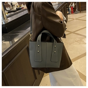 Détail d'un sac cabas en cuir gris foncé avec surpiqûres contrastées et clous sur un modèle