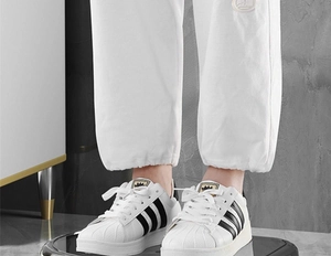Close-up of white shell-toe sneakers with black stripes and white jogger pants