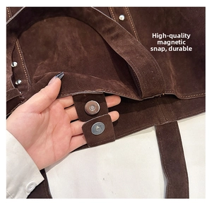 Detailed macro shot of the magnetic snap closure on a brown suede leather tote bag