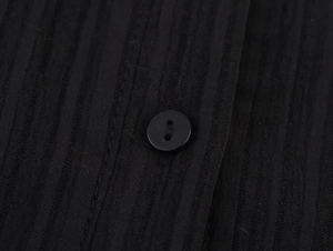 Détail d'un tissu noir à rayures verticales avec un bouton rond et des coutures fines