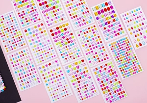 Flat lay of colorful acrylic rhinestone stickers in multiple shapes on pink background