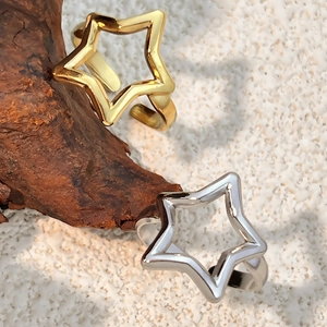 Minimalist gold and silver hollow star open rings on white sand with wood decor