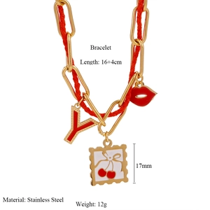 Detail showing red woven rope bracelet with gold letter Y, lip and cherry charms