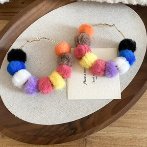Detail view of colorful faux fur pompom hoop earrings on a soft fabric display