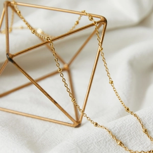 Gold plated stainless steel satellite chain necklace displayed on a geometric stand