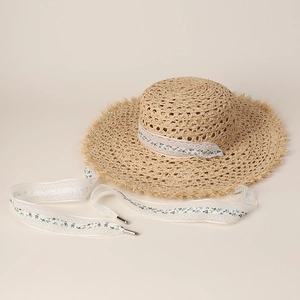Detail of beige raffia sun hat featuring floral lace ribbon and frayed edge brim
