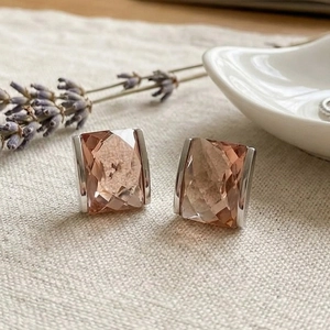 Detail of square-cut champagne glass earrings with 18K gold plating on linen background