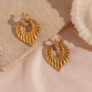 Macro view of gold-plated leaf drop earrings with sparkling crystals on stone texture