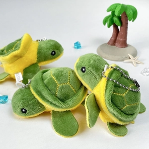 Three cute green turtle plush keychains with silver bead chains on a beach scene backdrop