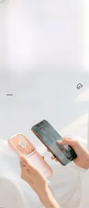 Pink foldable handheld fan used as a power bank to charge a smartphone on a desk