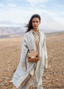 Brown leather moon-shaped handbag styled with linen coat in desert landscape setting
