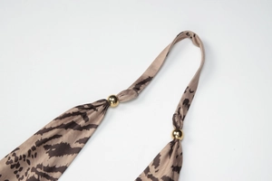 Détail de bretelles à motif léopard avec perles en métal doré et tissu synthétique