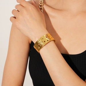 Close-up of a wide gold cuff bracelet featuring hammered texture and hollow cut-outs