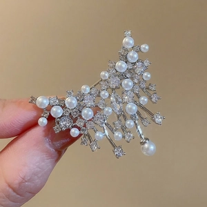 Elegant silver star brooch with pearls and rhinestones held by hand on a warm background