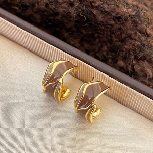 Detail of gold-tone C-shaped earrings with brown enamel on a soft velvet background