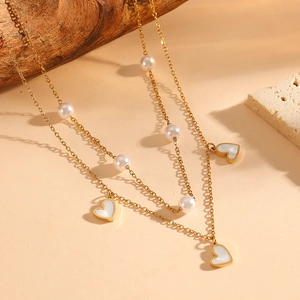 Gold double-layered necklace with white pearls and three heart-shaped pendants on stones