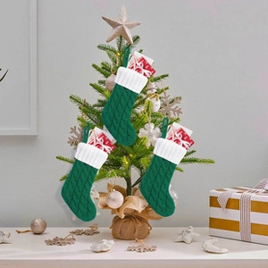 Three green knit Christmas stockings hanging on a festive tree with decorative gift boxes