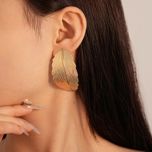 Close-up of a model wearing a large golden leaf-shaped metal stud earring with rich texture