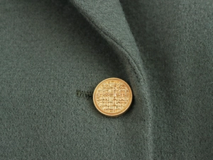 Detailed macro view of dark green wool texture and embossed gold button on coat