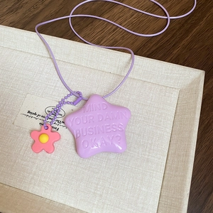 Dettaglio della collana con stella lilla, citazione a rilievo e ciondolo fiore rosa