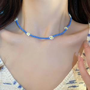 Close-up of handmade blue bead necklace with white daisy accents on collarbone