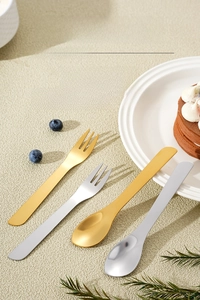 Macro shot of mirror-polished gold and silver dessert spoons and forks on a table
