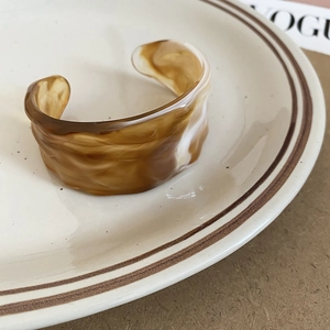 Detailed close-up of wide amber marble acrylic cuff bracelet with wavy texture on ceramic dish