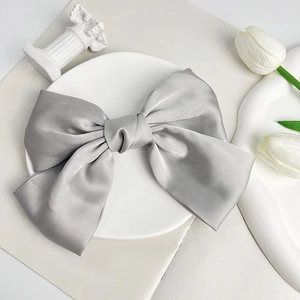 Close-up of silver-grey satin bow hair clip with elegant layered texture on white tray