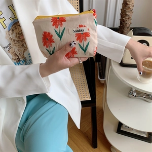 Detail of a beige floral makeup bag with red flowers and yellow zipper held by a model
