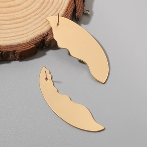 Macro detail of asymmetric gold crescent earrings with wavy texture on wooden display