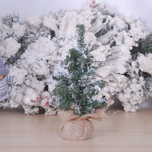 Miniature snow-flocked Christmas tree with rustic burlap base on wooden surface