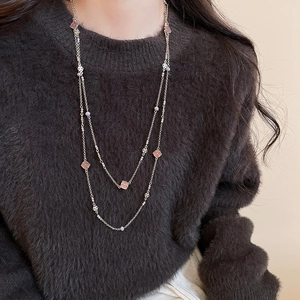 Detail of double-layer gold necklace with pink enamel and pearl on brown sweater