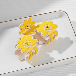 Elegant yellow floral hair claw clip with golden rhinestones on a white ceramic tray