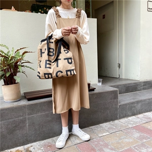 Detail of khaki pinafore dress and beige long sleeve shirt for casual street style