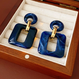 Detail of blue marble resin square earrings on a luxury wooden jewelry display