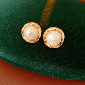 Close-up of vintage gold-plated round earrings with white lustrous center on green velvet