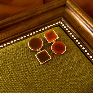 Detailed view of vintage gold-rimmed amber resin earrings on green fabric
