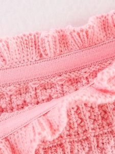 Close-up of pink knit dress detailing the elastic waistband and ruffled hem design