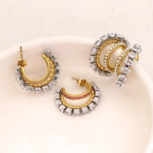 Detailed macro view of gold-plated C-shaped earrings with pink zircon and pearl accents
