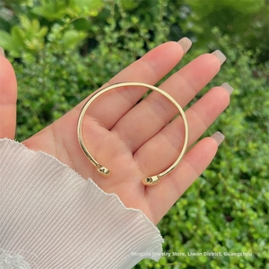 Dettaglio del bracciale rigido a C placcato oro 18K tenuto davanti al fogliame verde