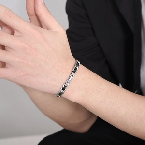 Bracelet gourmette NK en argent entrelacé de cuir noir porté par un homme en costume