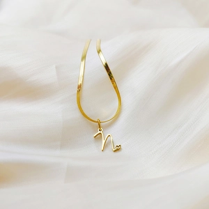 Detail of gold snake chain necklace featuring a cursive letter n pendant with a small heart