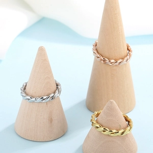 Detailed view of twisted rope rings in gold, silver, and rose gold on a wood stand