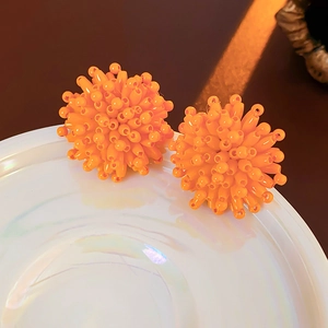 Macro shot of orange beaded spherical earrings on a white pearlescent decorative plate