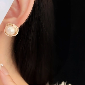 Close-up of rose gold hollow zircon earrings with large pearls on a model ear